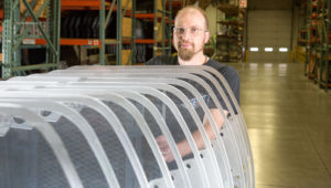 Worker handling curved polycarbonate transit windows in manufacturing facility