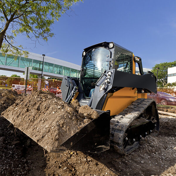 A compact track loader carrying dirt at a construction site, commonly used heavy equipment for efficient earthmoving and site preparation.
